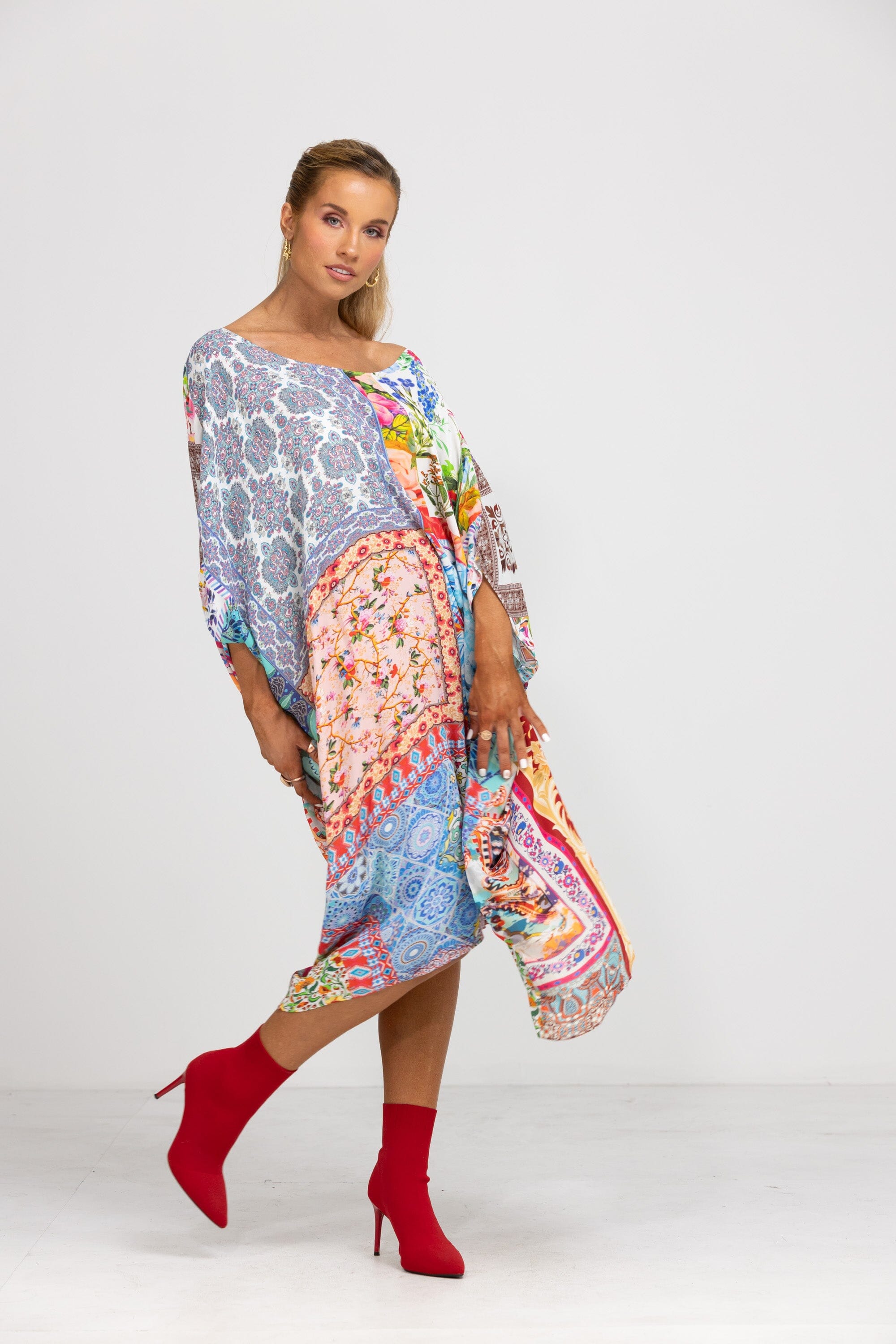 Bohemian-style Short Box Kaftan, Damascus print. The kaftan dress is worn with red knee-high boots, highlighting the asymmetrical, flowing hemline and the vibrant mix of blue, red, pink, and white prints.