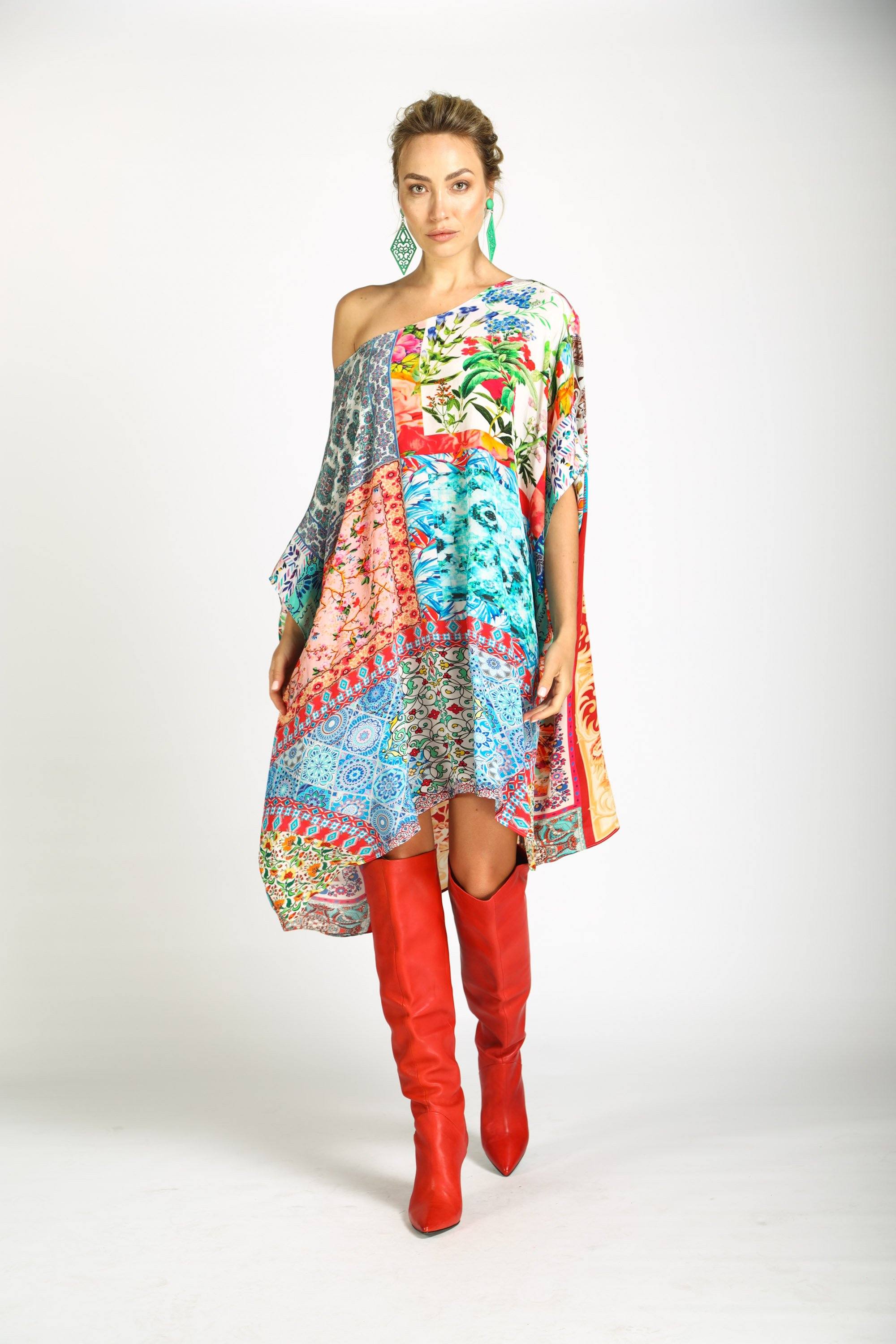 DAMASCUS - SHORT BOX KAFTAN by Bondi (TheSwankStore). A short, loose kaftan dress styled off-the-shoulder, featuring a vibrant, multicolored patchwork print with large floral, blue animal, and geometric sections, paired with red boots.
